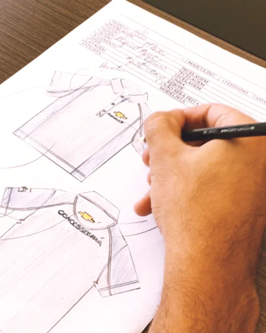 Mão desenhando a modelagem de uma camisa polo em papel