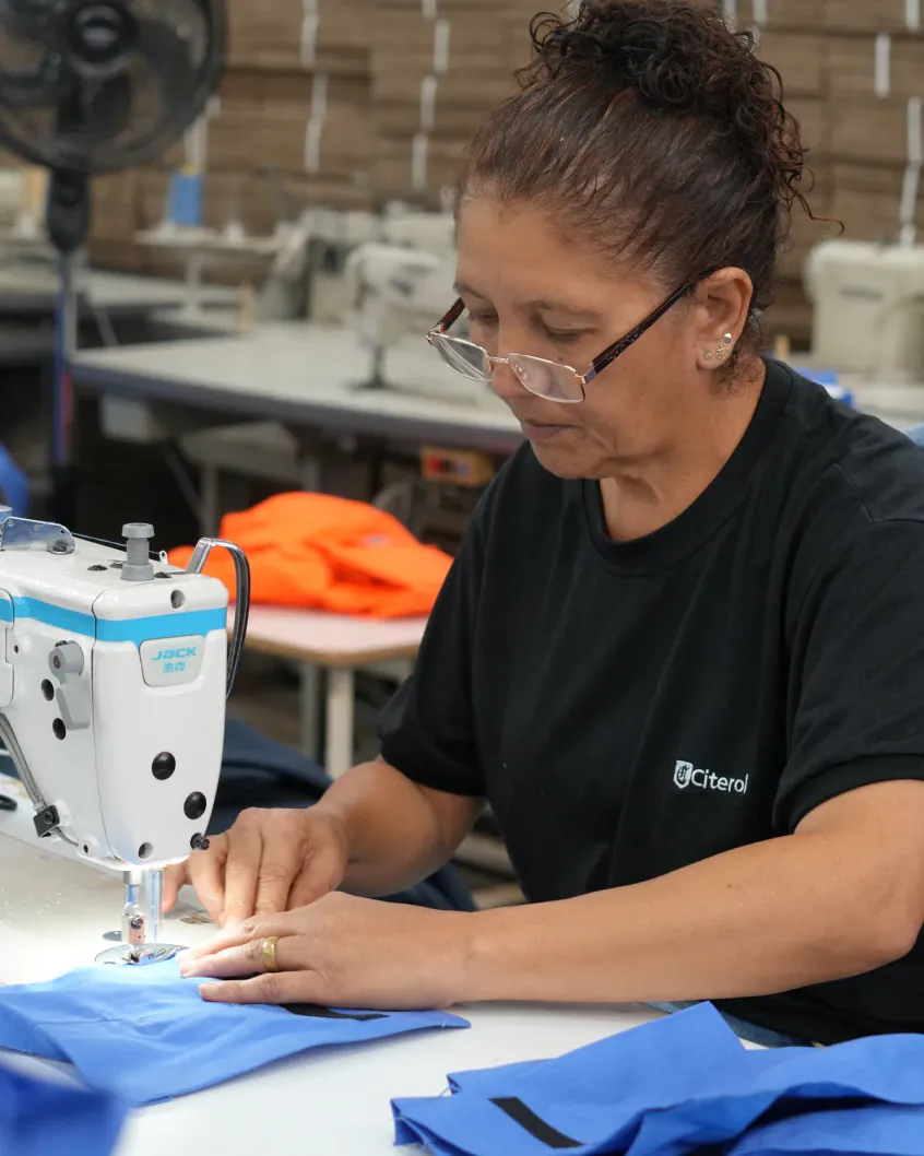 Costureira da Citerol na máquina, de uniforme preto, costurando uma peça azul